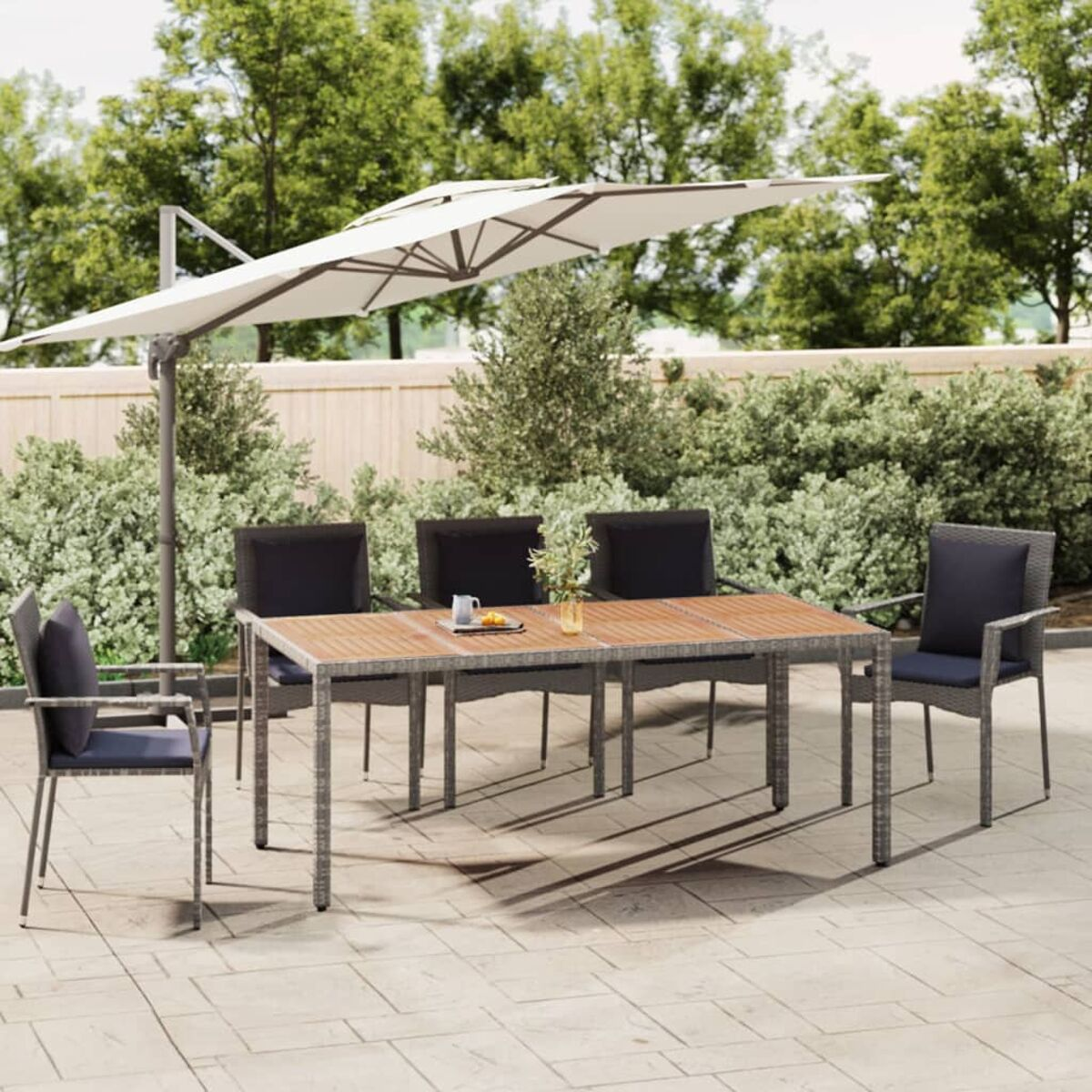 Essgruppe für den Außenbereich: Tisch, Stühle und Sonnenschirm. Tisch hat Holzplatte. Auf Terrassensteinen.