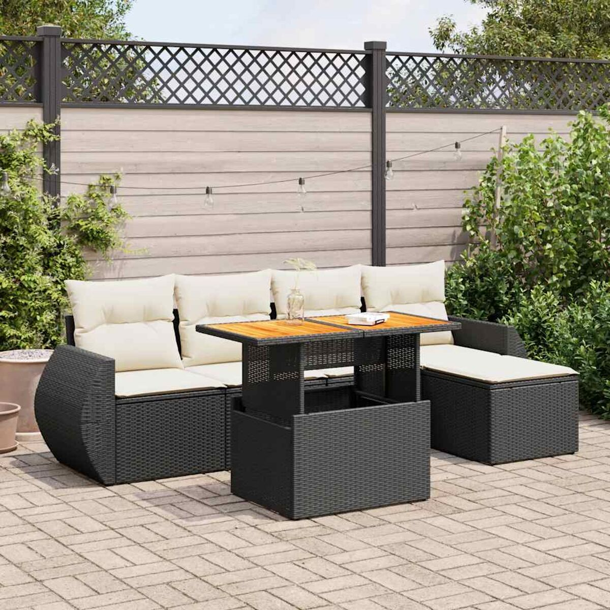 Set da patio all'aperto con mobili neri, un tavolo di legno e cuscini beige. Una recinzione e piante sono sullo sfondo.