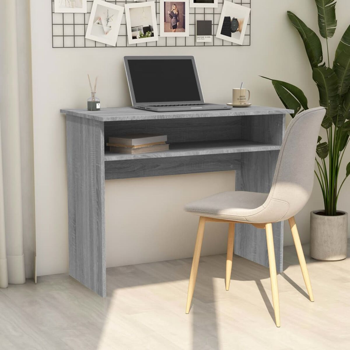 Grauer Schreibtisch mit Laptop, Büchern und Stuhl. Eine Pflanze steht daneben.