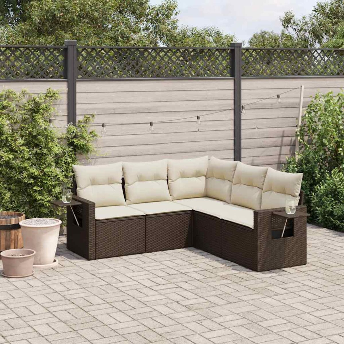 Ein Outdoor-Ecksofa mit cremefarbenen Kissen. Es steht auf einer Ziegelterrasse, mit Pflanzen und Holzzaun im Hintergrund.