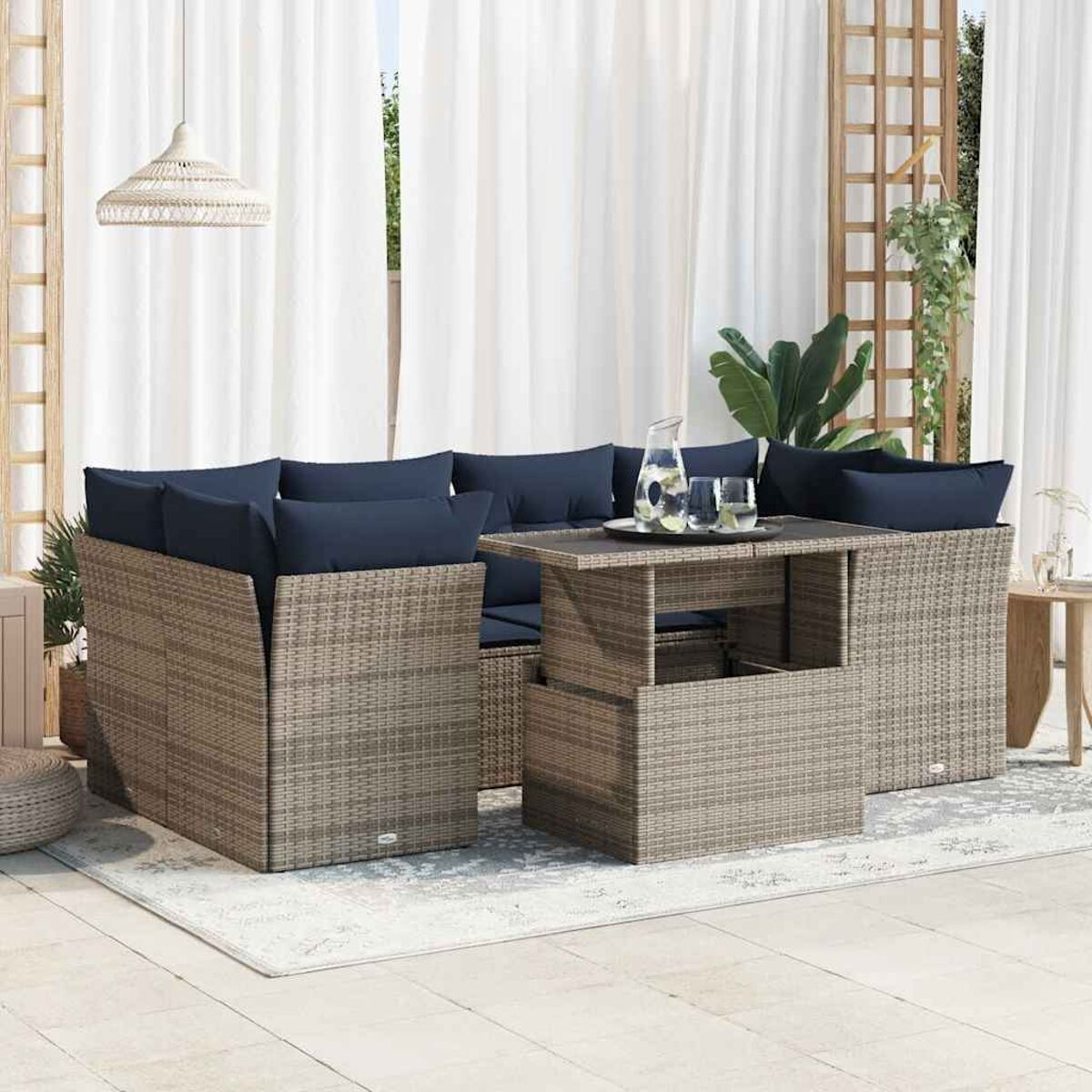 Set living esterno in un contesto patio. Arredamento in vimini con cuscini blu navy, tende bianche.