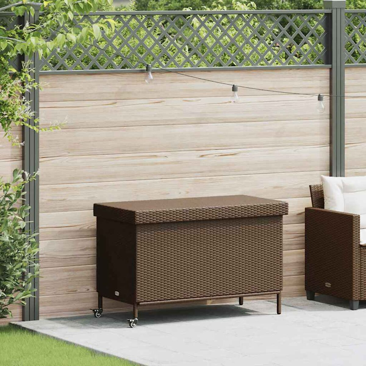 Eine braune gewebte Aufbewahrungsbox mit Rädern auf einer Terrasse, mit Zaun und Gras im Hintergrund.