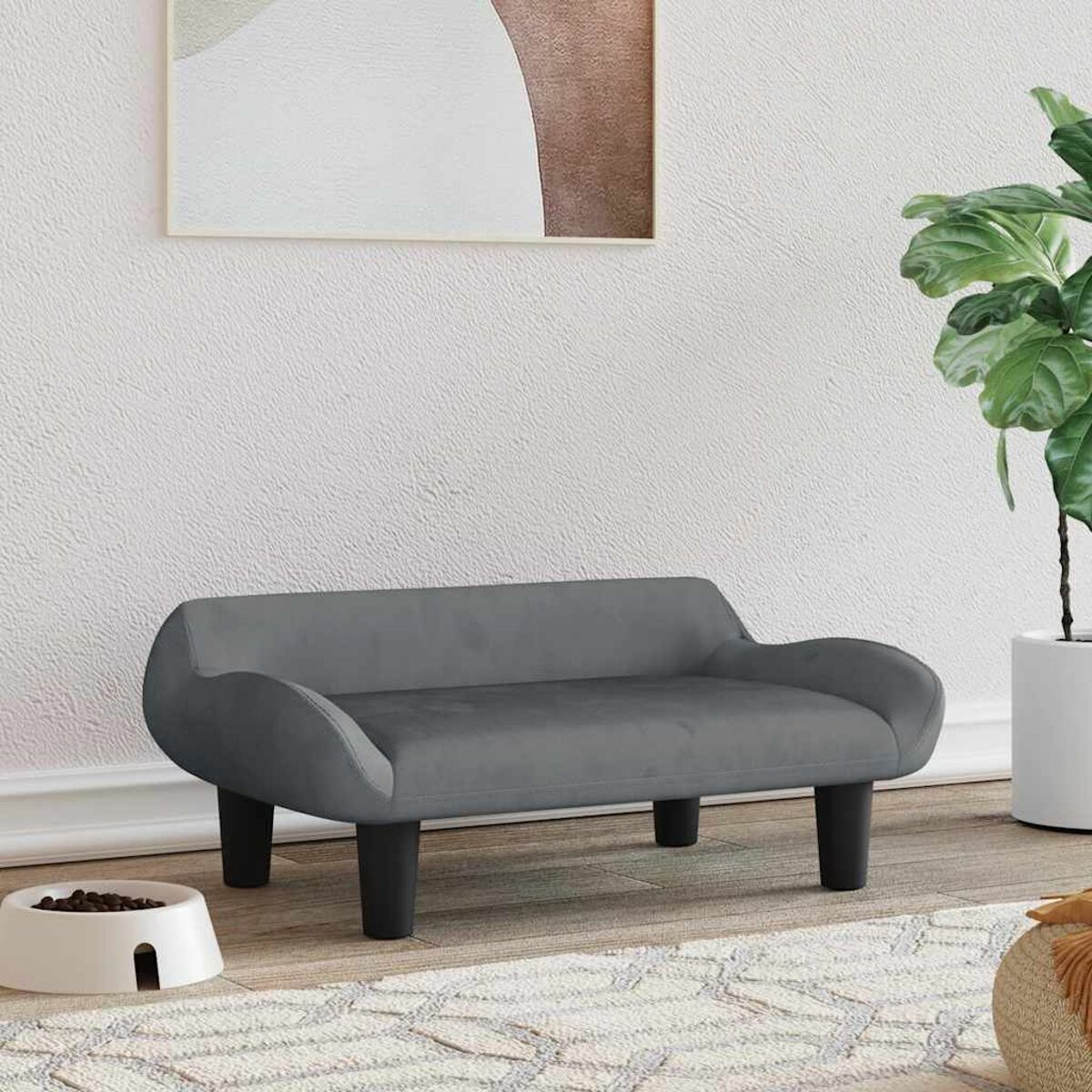 Ein graues Hundebett auf einem Teppich in einem Raum mit Pflanze und Kunst.