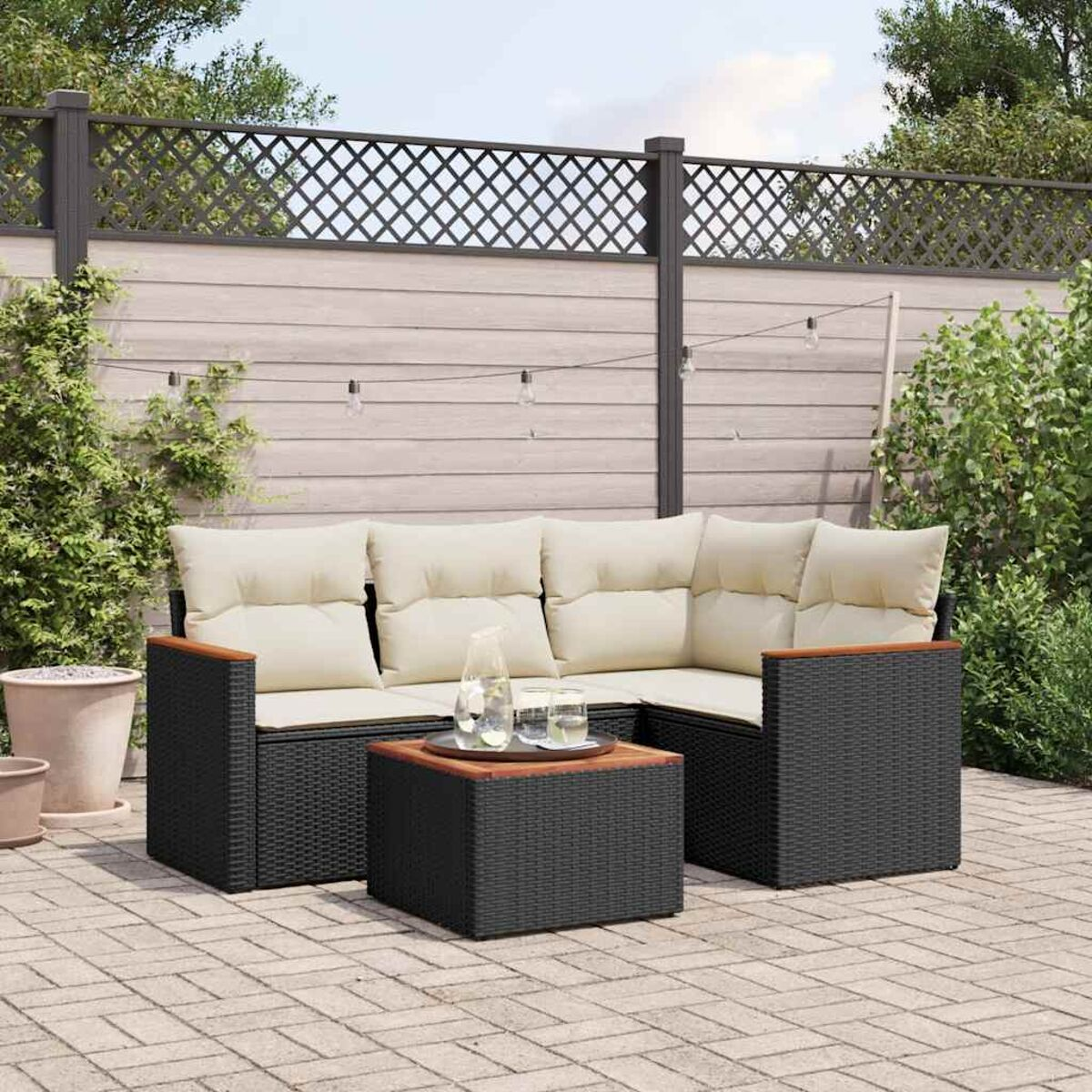 Schwarzes Outdoor-Ecksofa aus Korbgeflecht mit cremefarbenen Kissen und einem quadratischen Tisch.