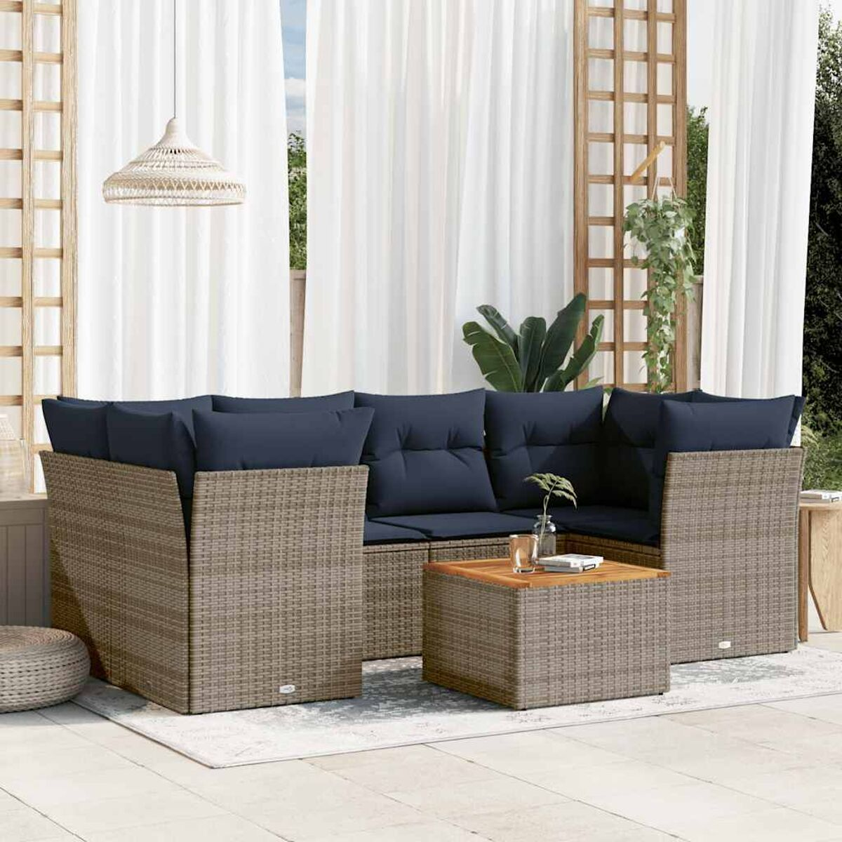 Set divani in rattan da esterno con cuscini blu navy, tavolo in legno e tende bianche sullo sfondo.