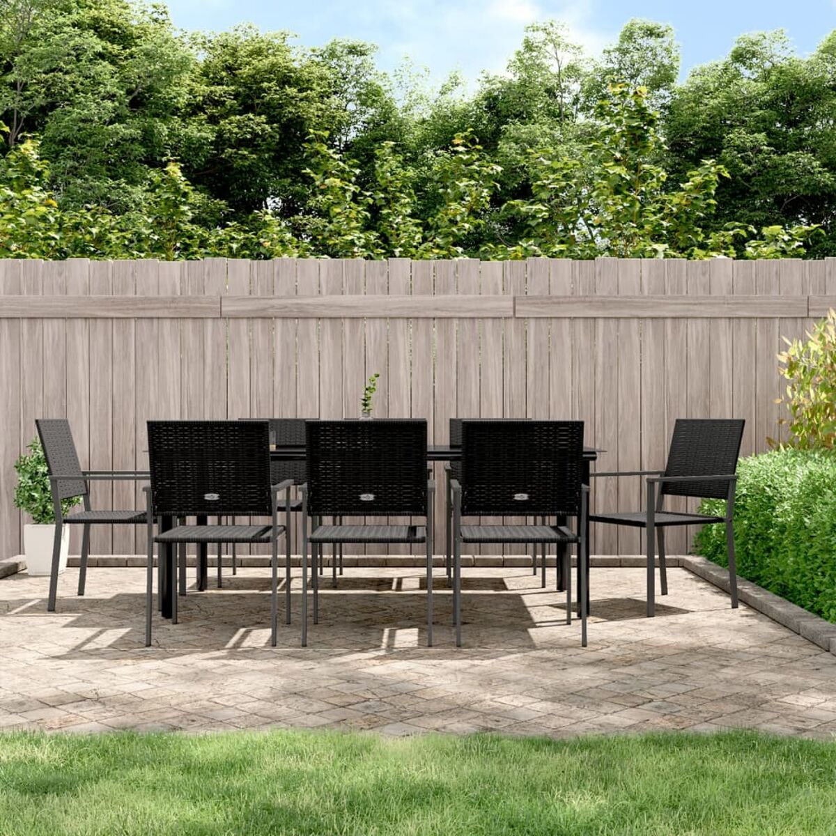 Outdoor-Essgruppe: Tisch, 6 Stühle auf einer Terrasse. Grünes Gras, Holzzaun, Bäume im Hintergrund.