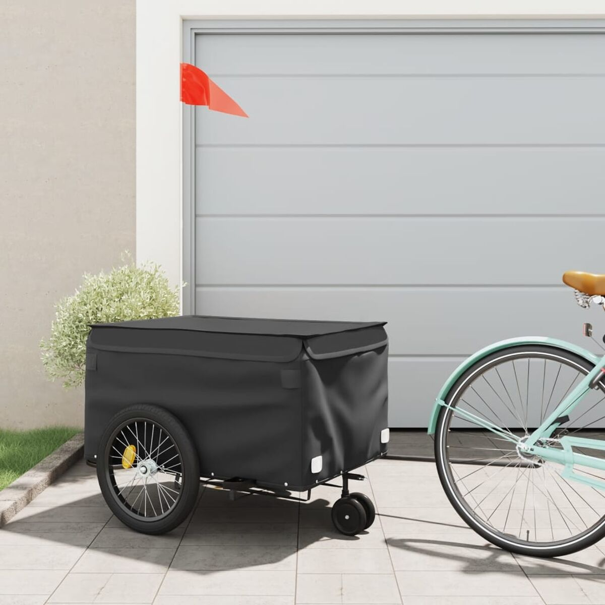 Ein schwarzer Fahrradanhänger mit roter Fahne, geparkt vor einem Garagentor. Ein Fahrrad ist teilweise rechts sichtbar.