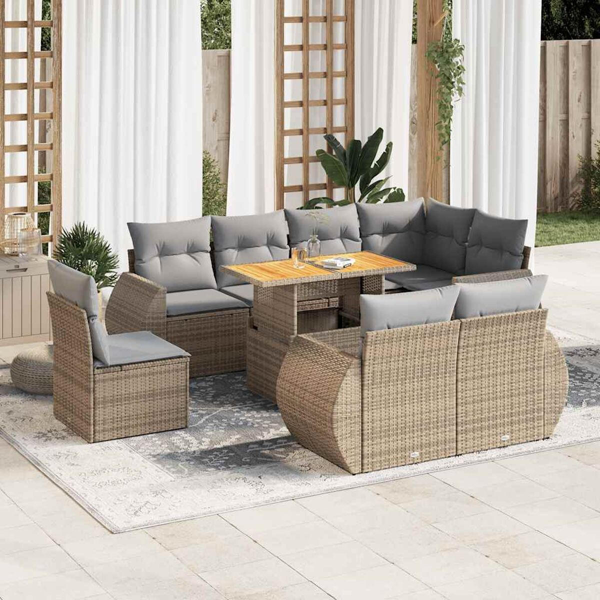 Set da esterno in rattan beige con cuscini grigi, tavolo su tappeto e tende bianche.