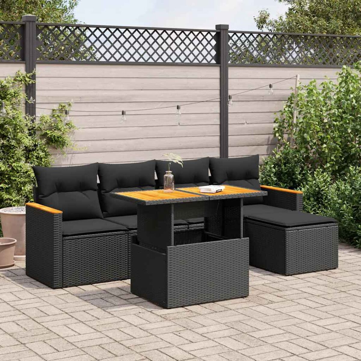 Un set da esterno in rattan nero con tavolo, divano e pouf. In un giardino.
