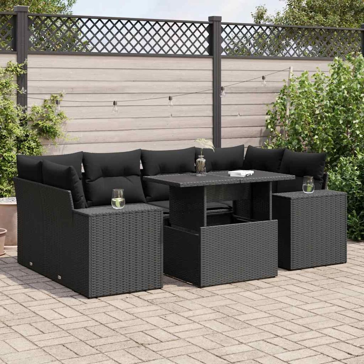 Set di mobili da esterno in vimini nero con tavolo, divano e tavolino. Patio in mattoni e verde.