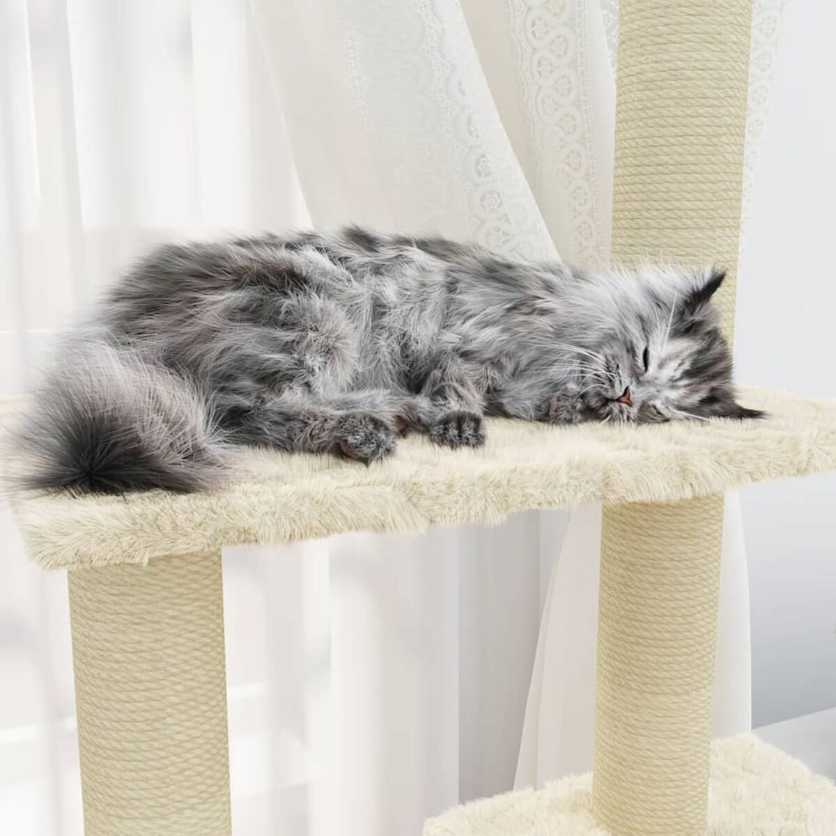 Eine flauschige graue Katze schläft auf einer beigen Katzenbaumplattform. Weiße Vorhänge sind im Hintergrund.