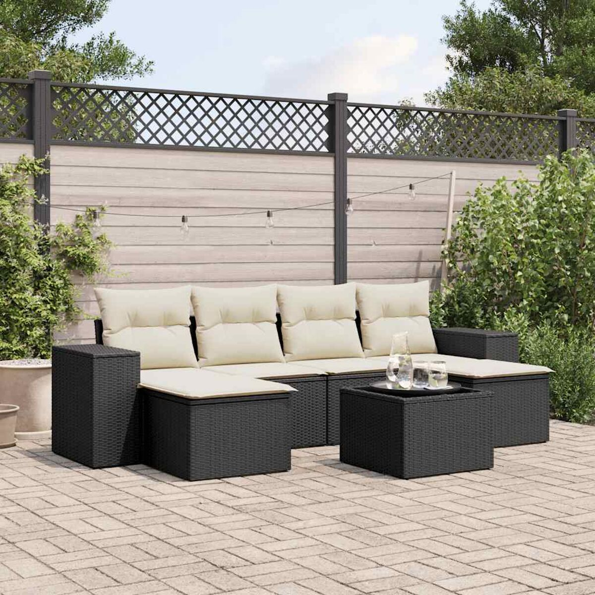 Terrasse mit schwarzem Korbsessel, beigen Kissen und Tisch.
