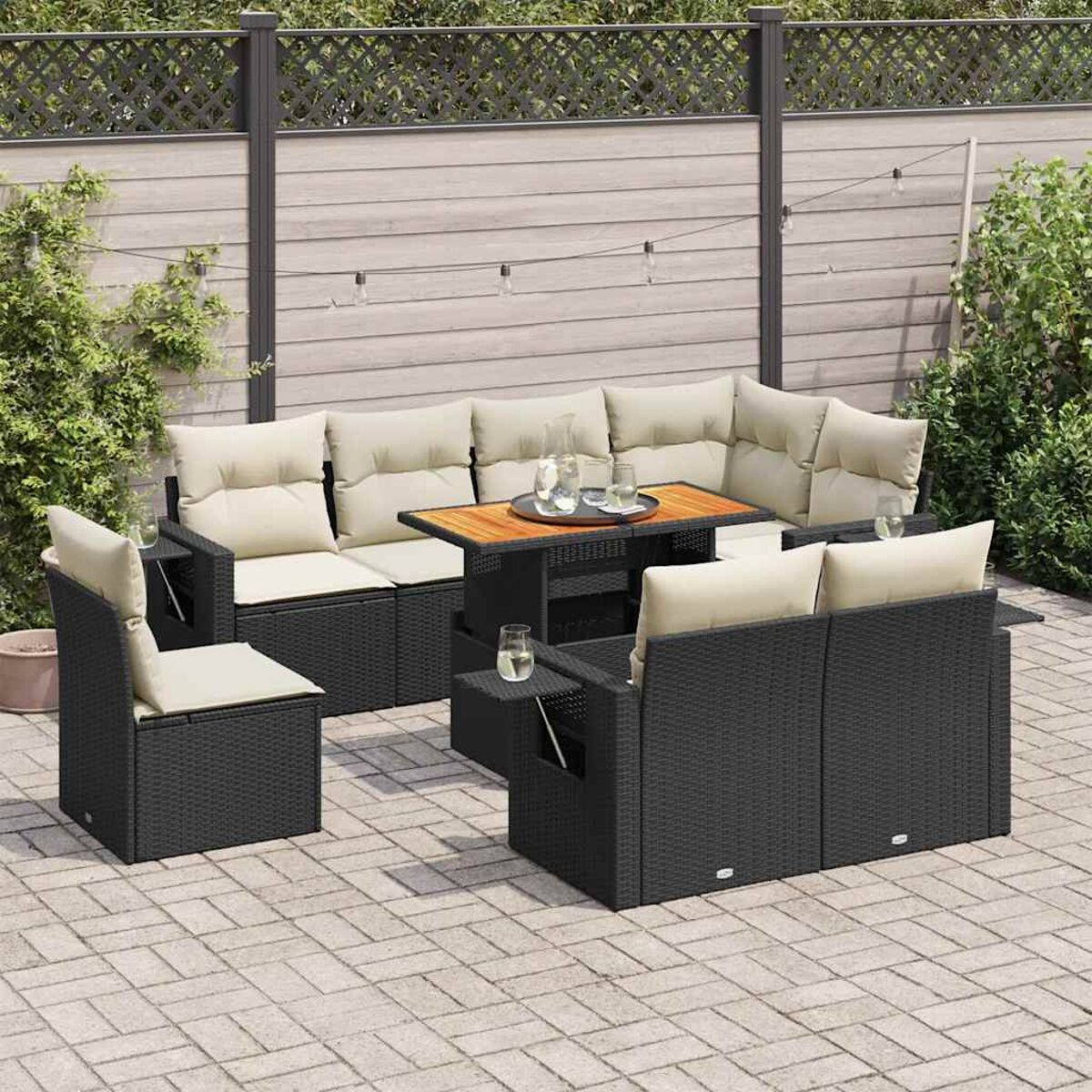 Set divani in rattan da esterno con cuscini beige, tavolo in vetro e un patio con fogliame verde.