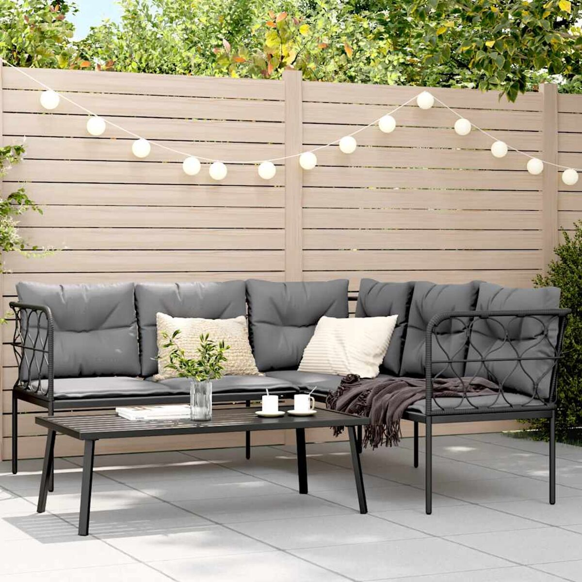 Outdoor-Ecksofa mit grauen Kissen, einem Couchtisch und im Hintergrund ein Holzzaun und Pflanzen.