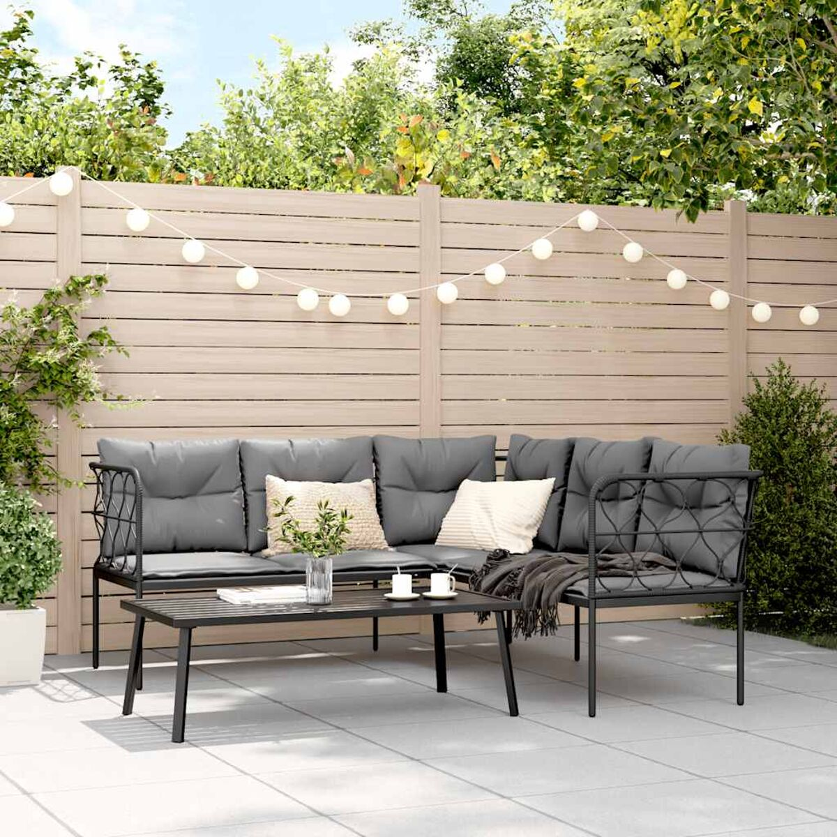 Outdoor-Sitzarrangement: schwarzes Metallsofa und Tisch, mit Kissen und Lichtern.