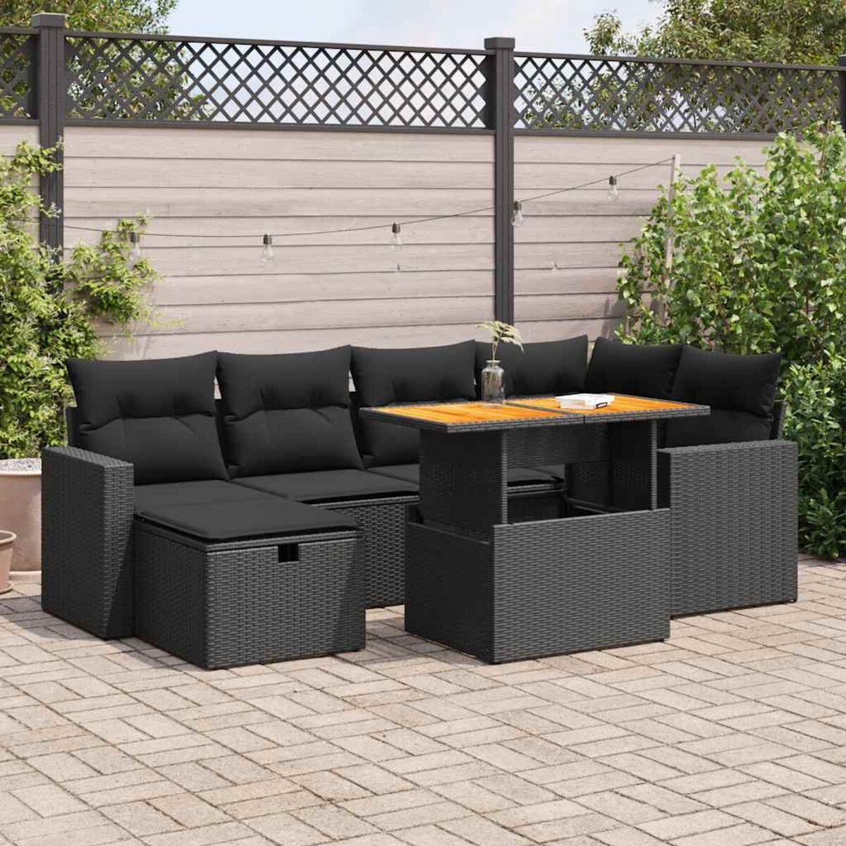 Set divano da esterno nero con tavolo. Aspetto vimini. Patio in mattoni e recinzione sullo sfondo.