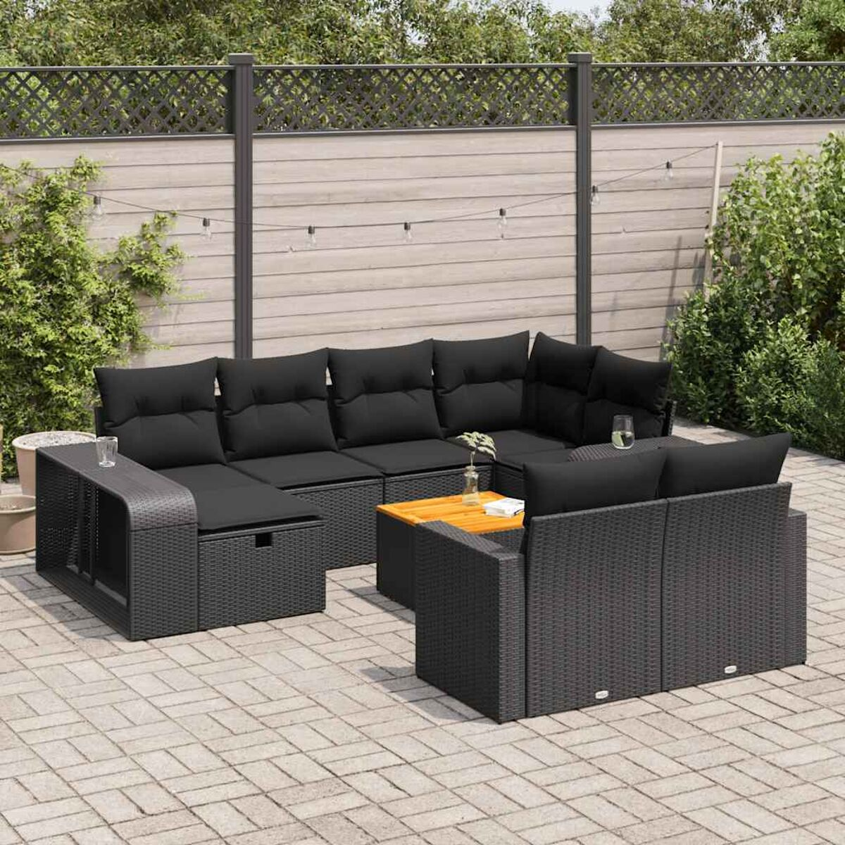 Eine schwarze Rattan-Sitzgruppe im Freien. Enthält ein Ecksofa, einen Tisch und einen Stuhl. Schwarze Kissen.