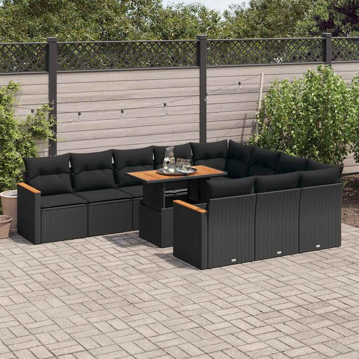 Set divani in vimini nero per esterni. Include un divano angolare, tavolo e sedute aggiuntive. Su un patio in mattoni.