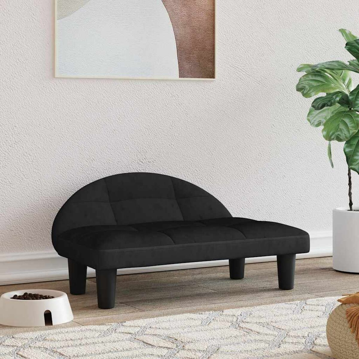 Ein kleines schwarzes Haustiersofa, platziert auf einem Teppich vor einer Wand mit einem Gemälde und einer Pflanze.