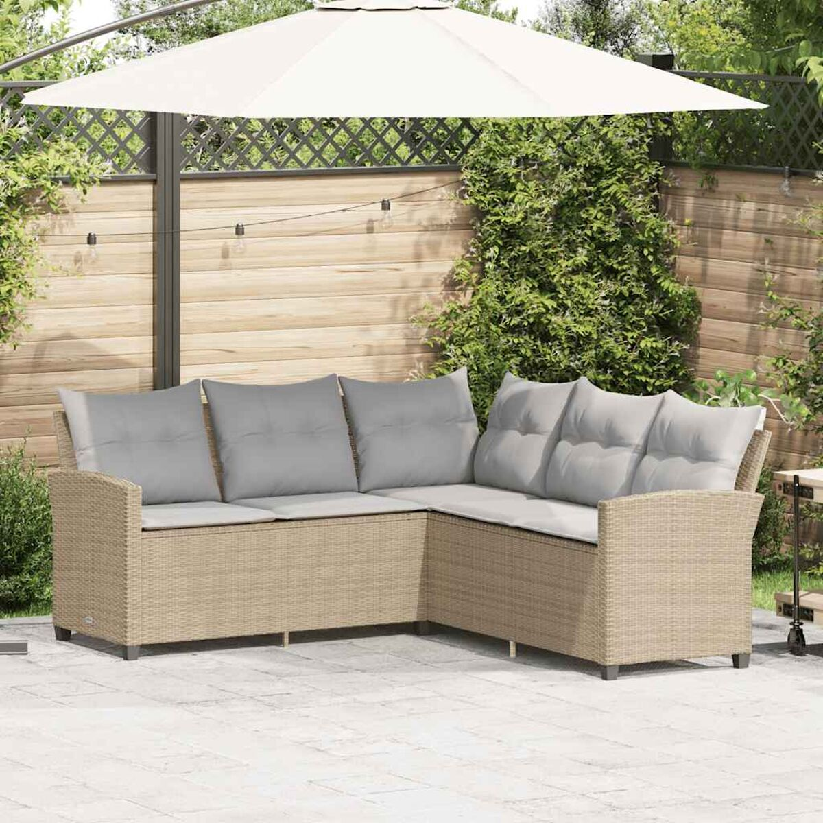 Divano angolare in rattan da esterno con cuscini grigi sotto un ombrello bianco, su un patio.