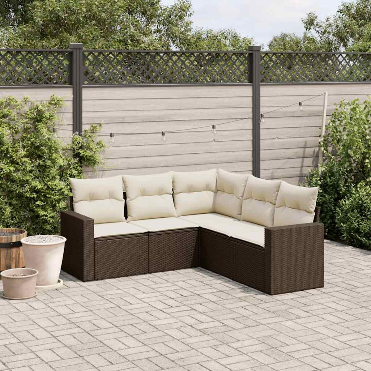 Braunes Gartenmöbel-Set auf Pflastersteinen, mit beigen Kissen. Im Hintergrund sind ein Zaun und Pflanzen.