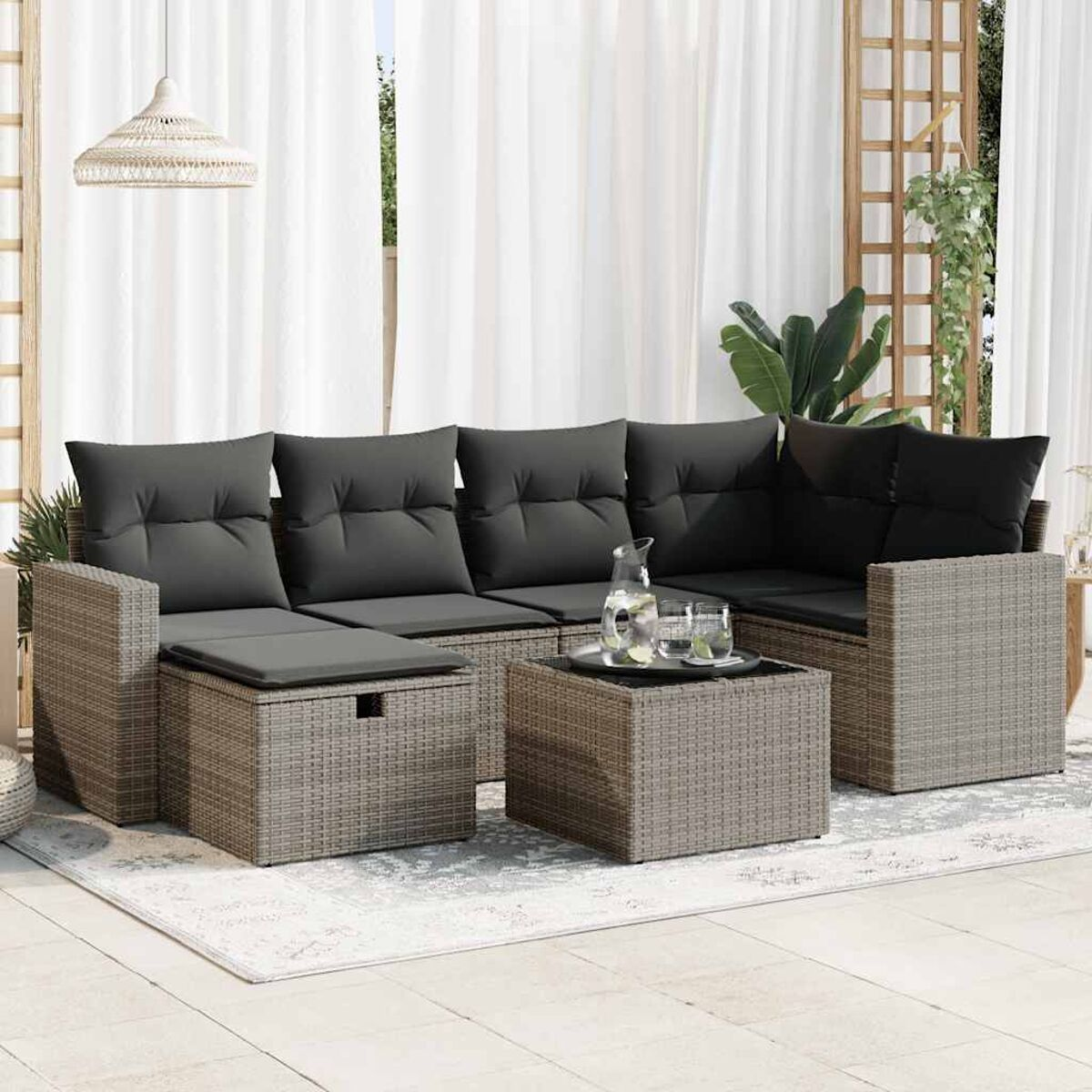 Outdoor-Ecksofa-Set mit grauen Kissen, einem Tisch, einem Teppich und weißen Vorhängen.