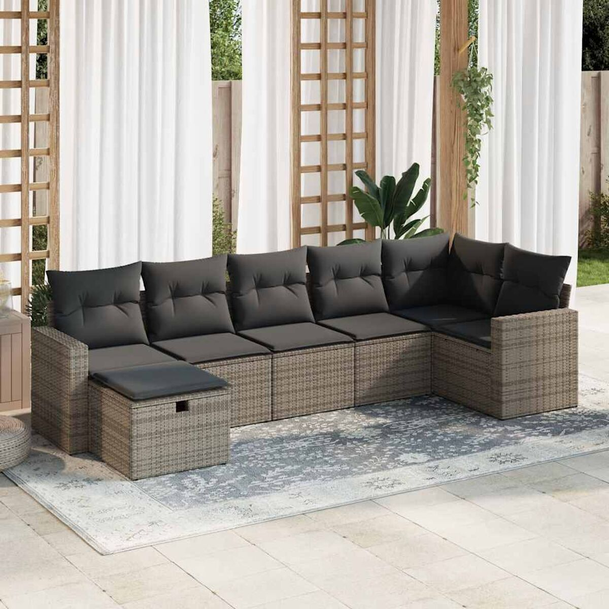 L-förmiges Outdoor-Sofa mit grauen Kissen, auf einem gemusterten Teppich, mit weißen Vorhängen im Hintergrund.