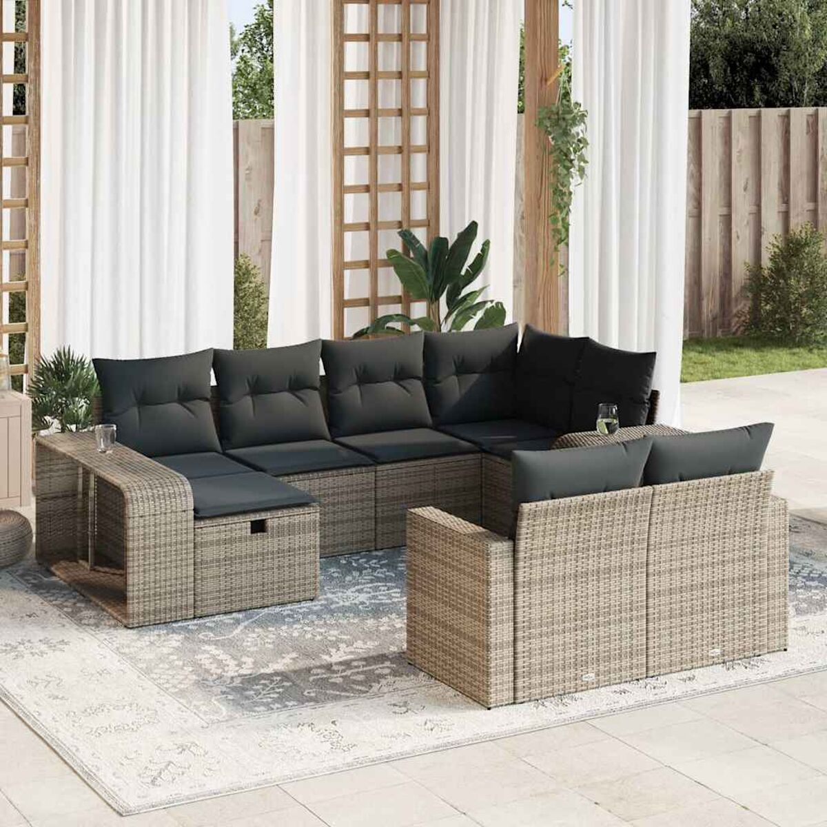 Geflochtenes Outdoor-Sitzensemble auf einem Teppich. Sofa und Stühle mit grauen Kissen, Gläser.