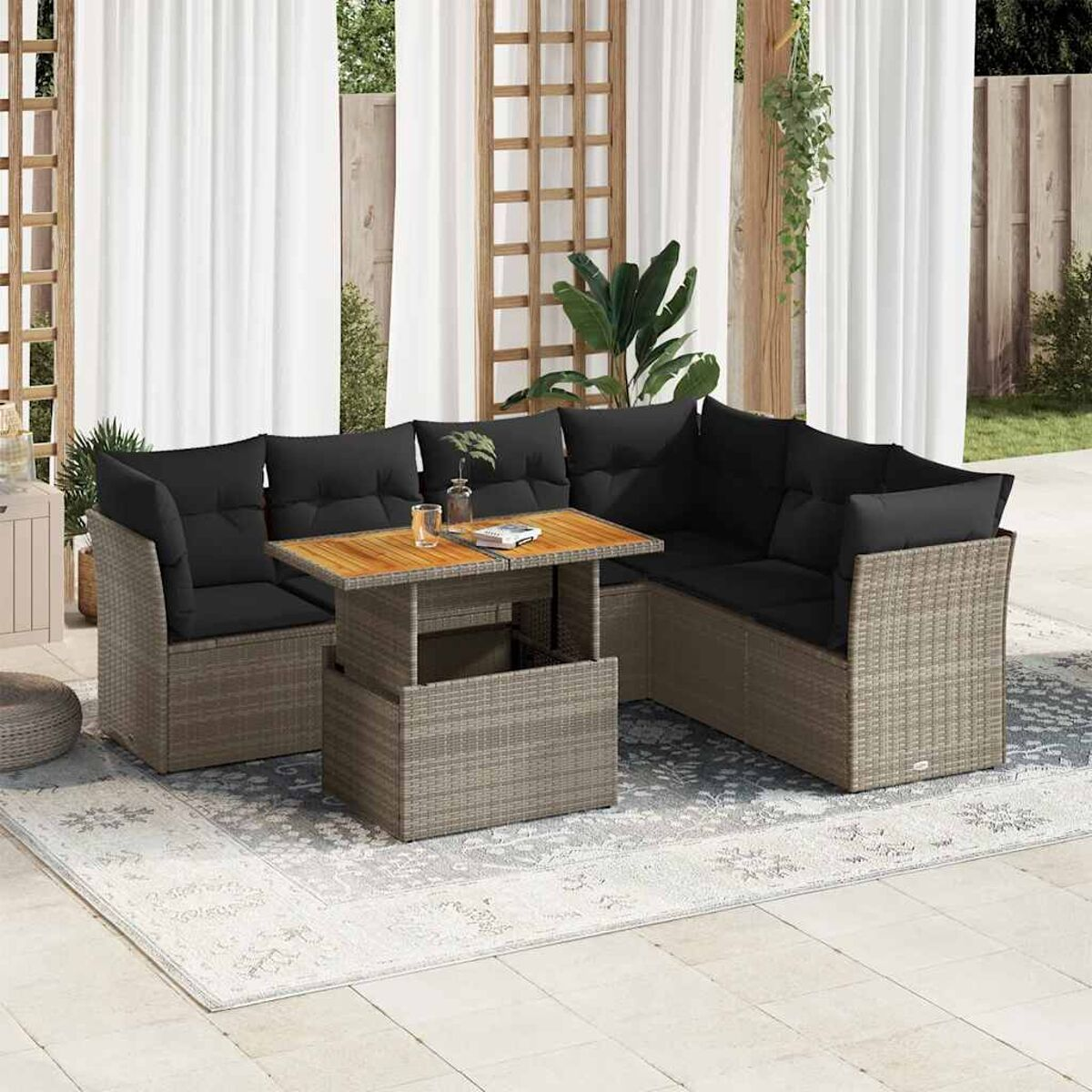 Divano esterno in rattan con cuscini neri e un tavolo in legno su un tappeto fantasia. La scena è su un patio.