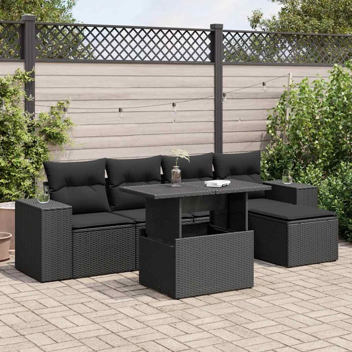 Set di divani da esterno in rattan nero con cuscini neri e un tavolo, su un patio pavimentato.