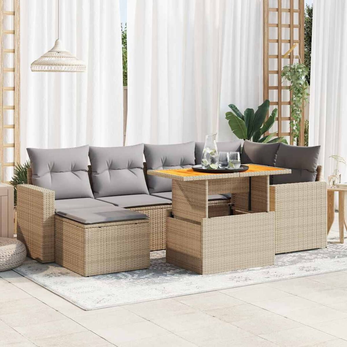 Outdoor-Setting mit grauem Rattansofa und Tisch. Weiße Vorhänge und Pflanzen sichtbar. Sonnig.