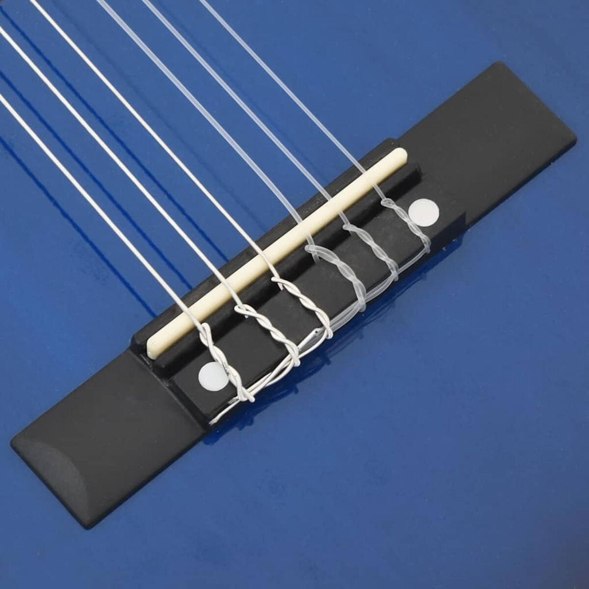 Nahaufnahme eines Gitarrenstegs. Saiten sind über einen schwarzen Steg gespannt. Steg ist auf blauer Oberfläche.