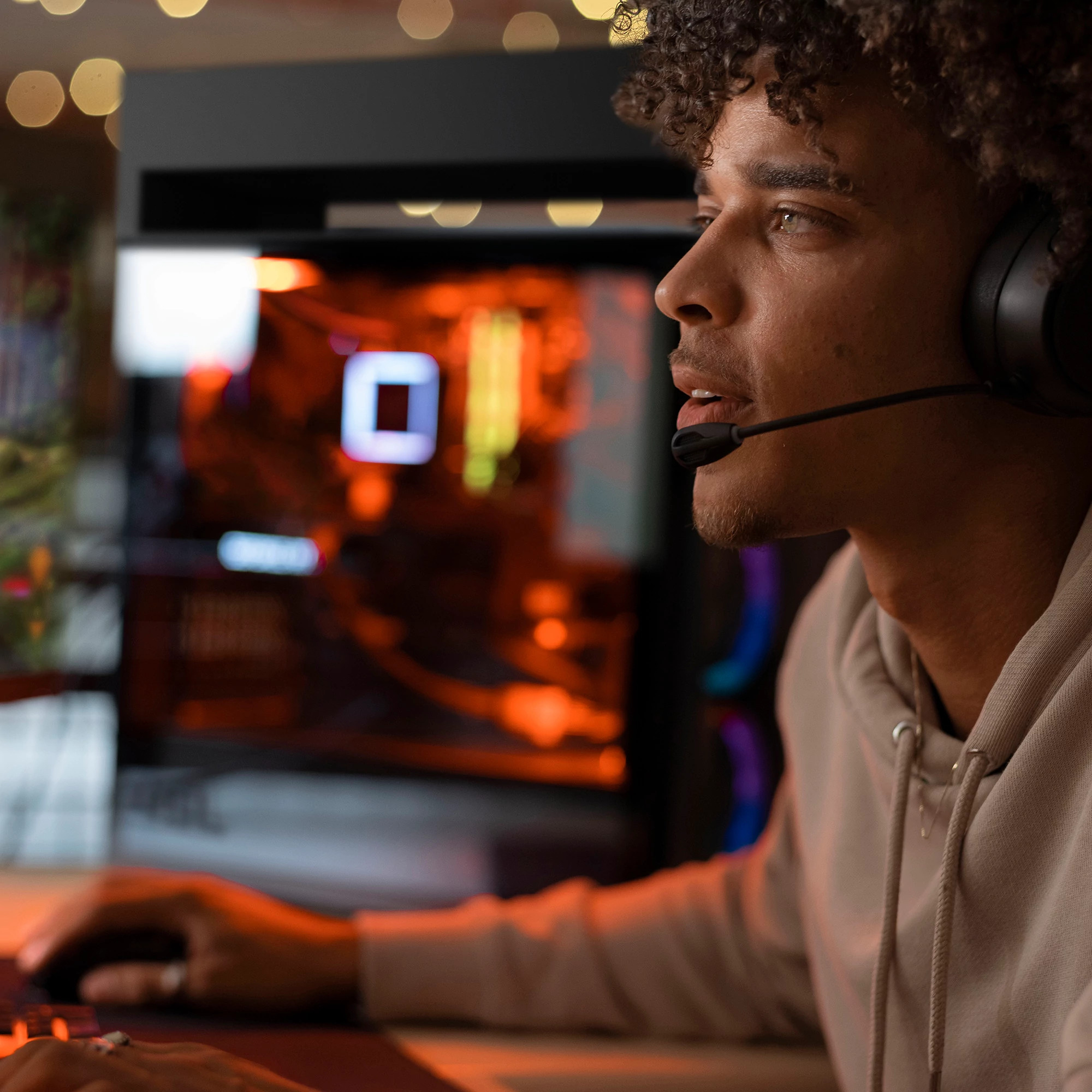 Mężczyzna w słuchawkach, grający na komputerze. Tło jest podświetlone pomarańczowymi odcieniami.