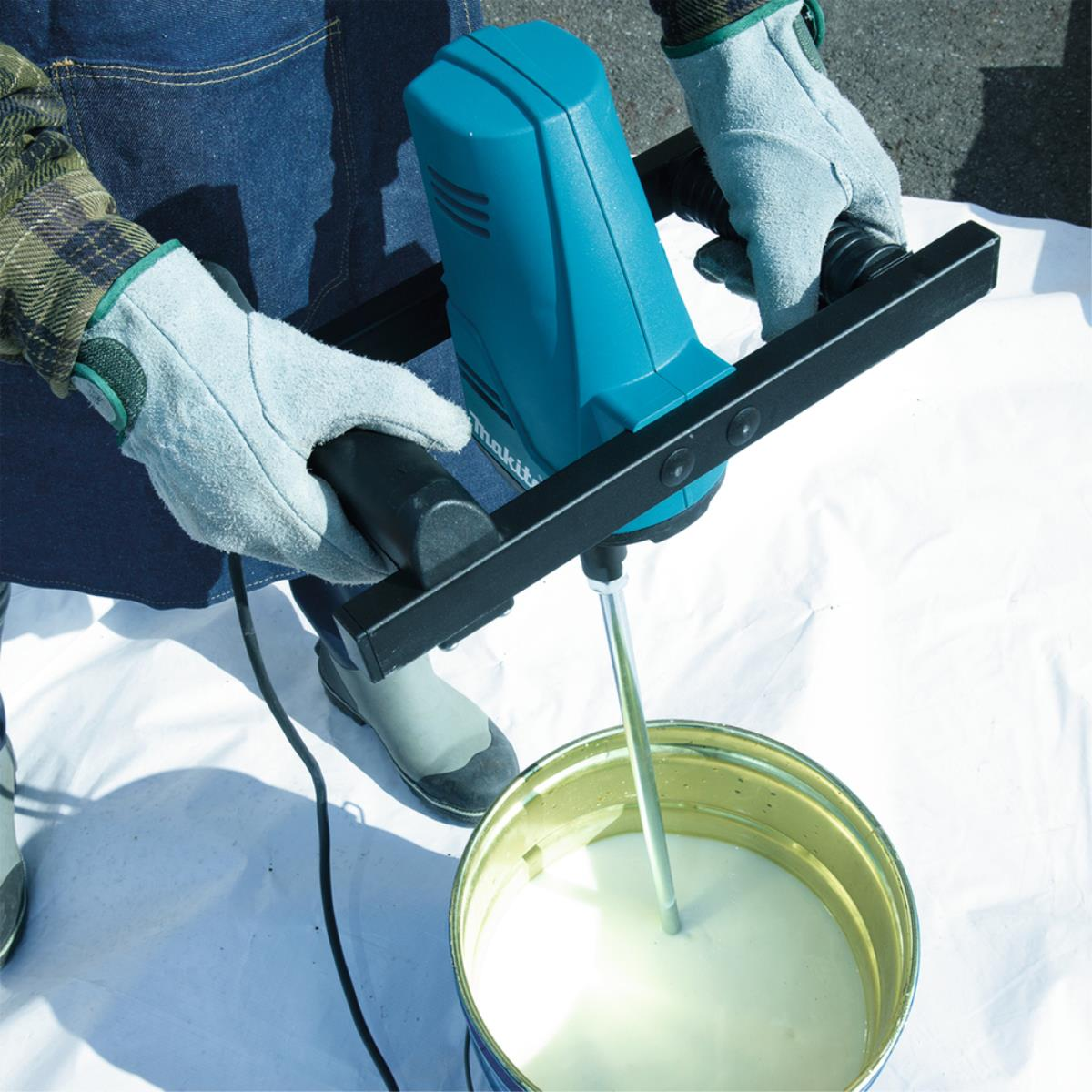 Persona che usa un utensile Makita blu per mescolare liquido in un secchio di metallo.