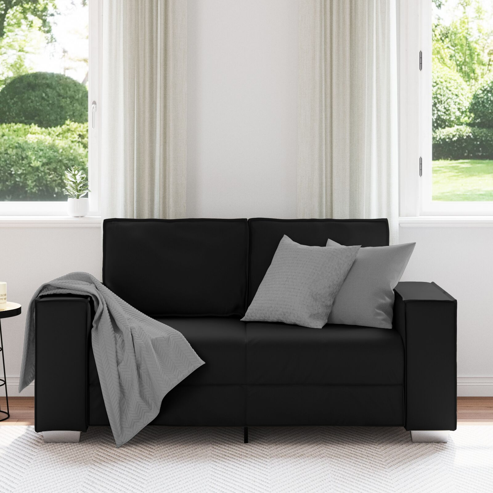 Schwarzes Sofa mit grauen Kissen und Decke. Weißer Teppich und Fenster mit natürlichem Licht.