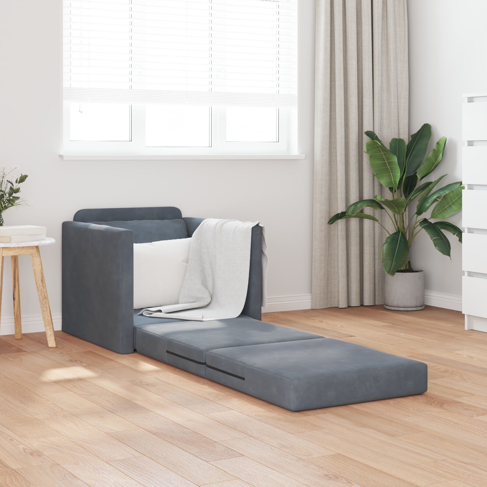Klappbares Schlafsofa, dunkelgrau, mit weißem Kissen und Decke. Auf Holzboden.