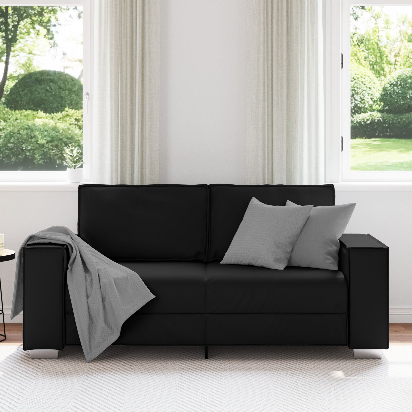 Ein schwarzes Ledersofa mit zwei grauen Kissen, einer grauen Decke und einem Beistelltisch.