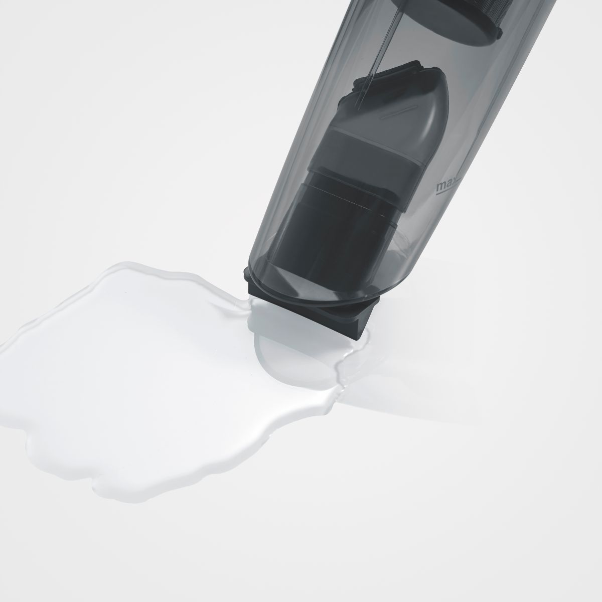 Depósito transparente de aspiradora con derrame de agua en superficie blanca.