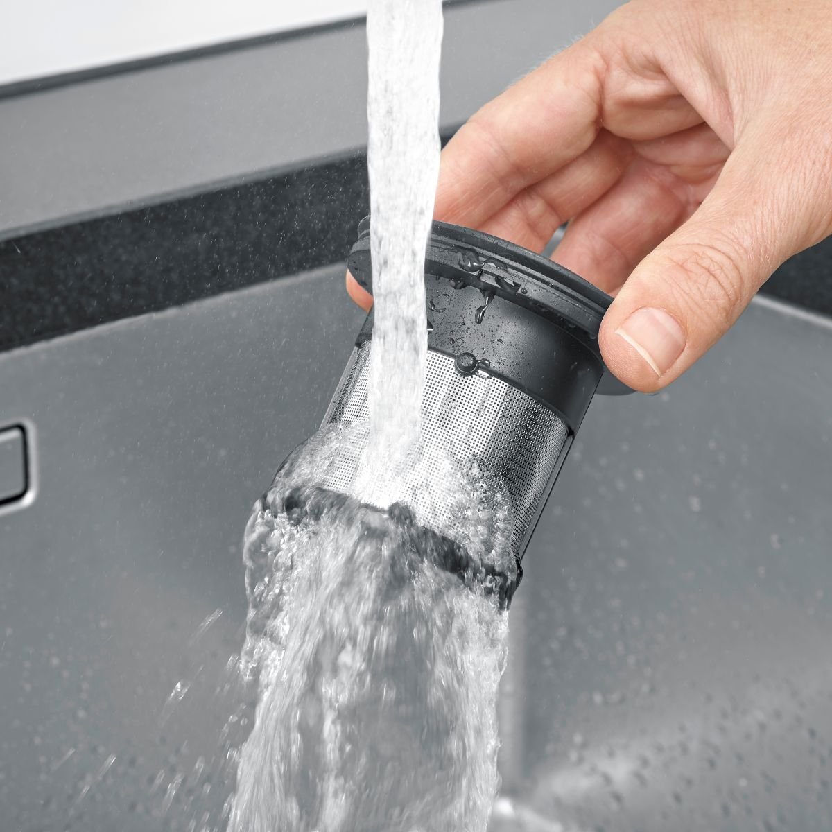 Mano sosteniendo un filtro negro, agua vertiéndose de un grifo a un fregadero.