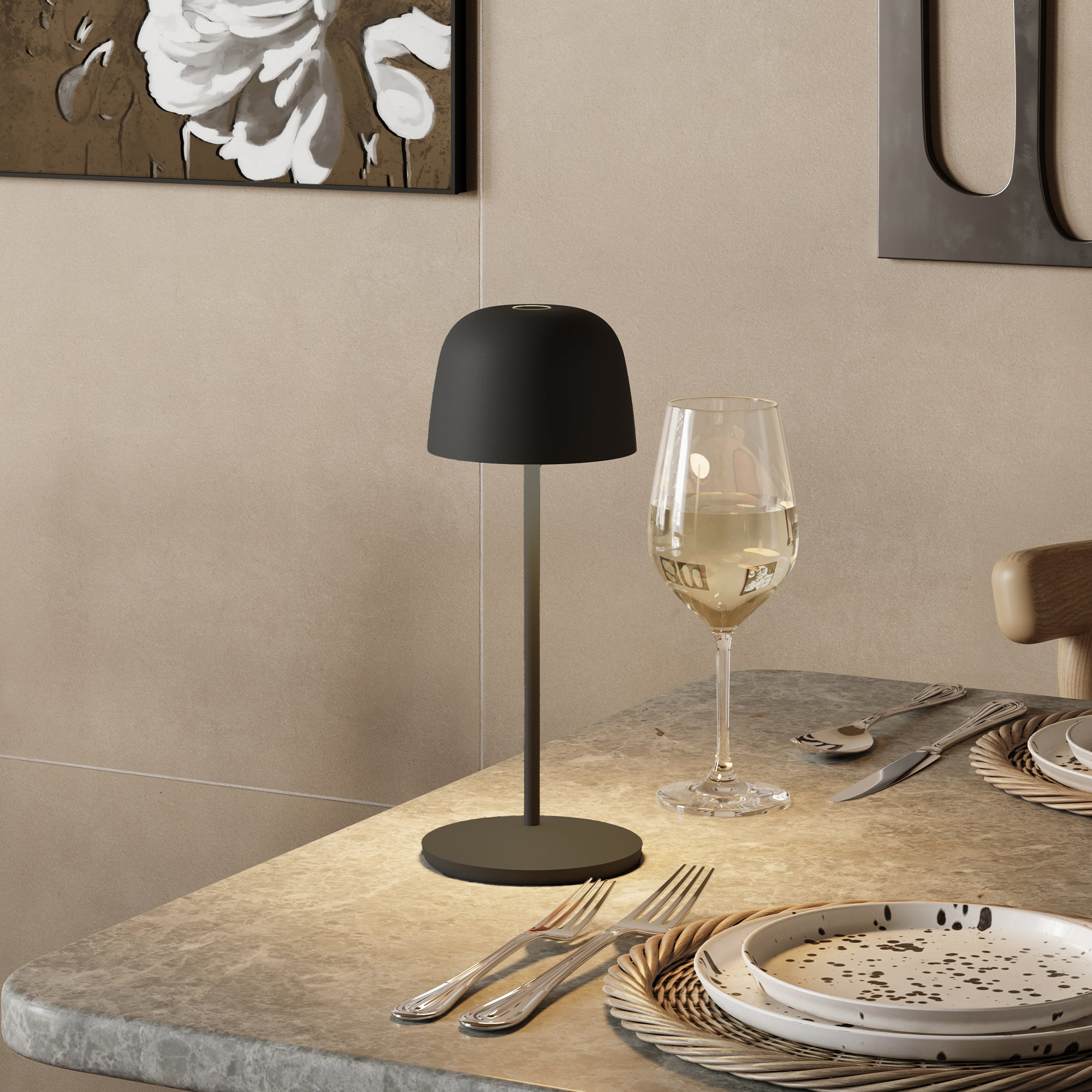Schwarze Tischlampe und Weinglas auf einem Tisch. Beige Wand und Teller im Hintergrund.