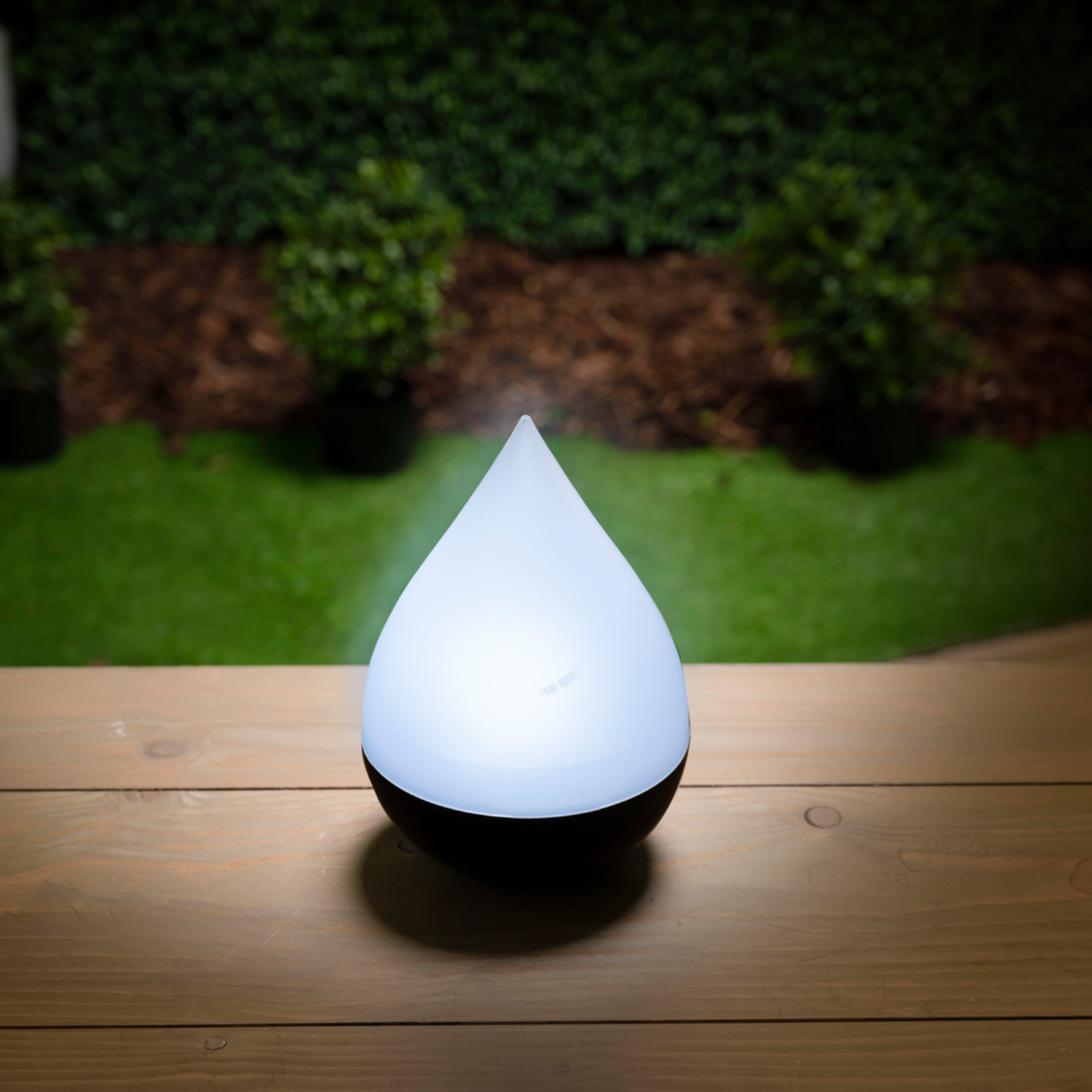 Druppelvormige lamp brandt, op houten oppervlak, met groene achtergrond.