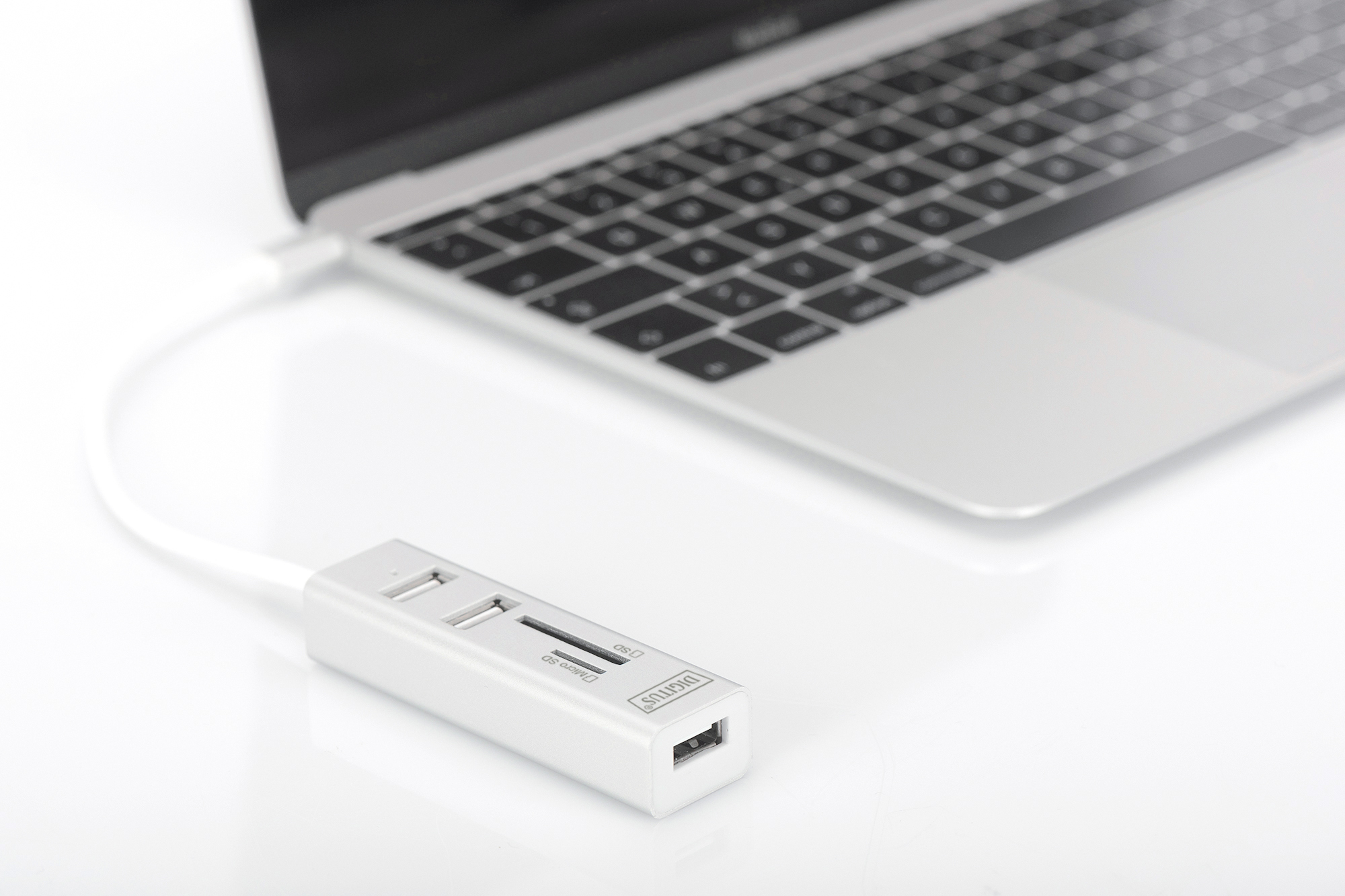 Laptop i biały hub USB-C. Hub posiada porty USB, kart SD i Ethernet.