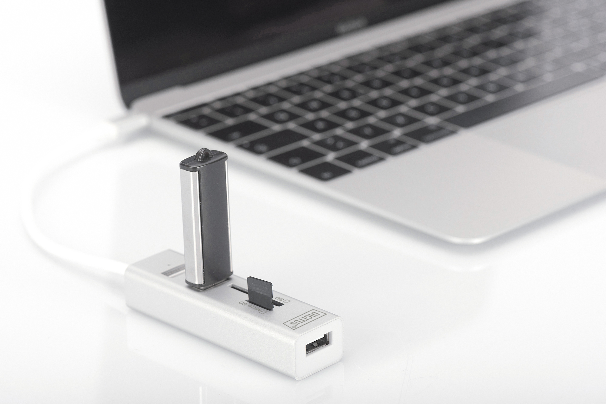 Srebrny hub USB z portem USB, gniazdem kart SD i podłączonym napędem flash USB. Za nim jest laptop.