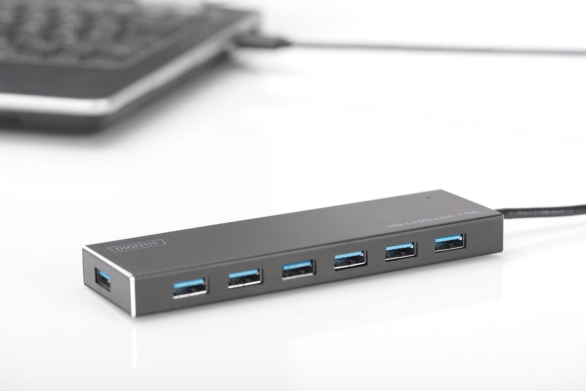 Bir dizüstü bilgisayara bağlı yedi mavi USB portlu siyah bir USB 3.0 hub, beyaz yüzey.