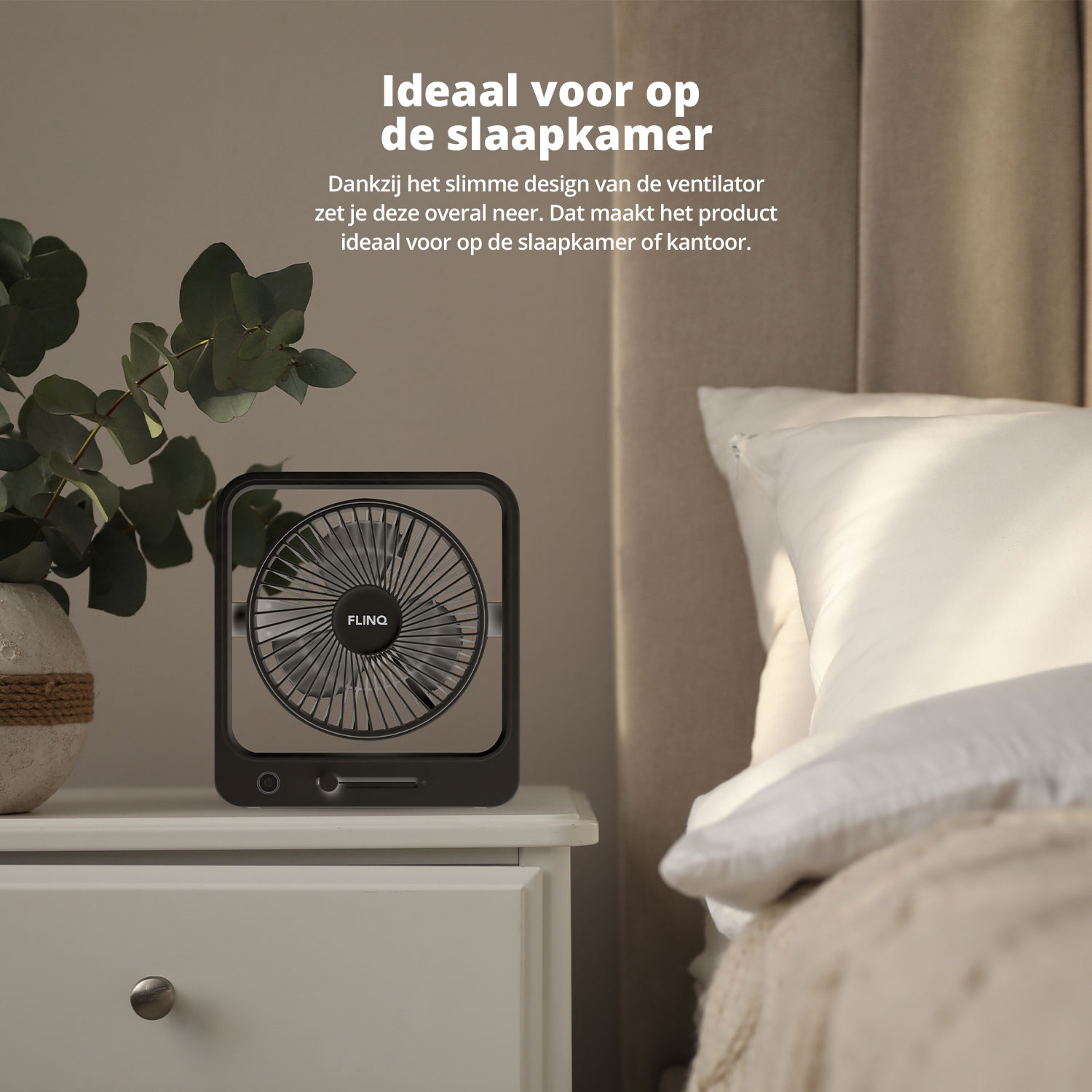 Ventilateur carré noir sur une table de chevet blanche, à côté d'un lit avec un oreiller blanc et une plante verte.