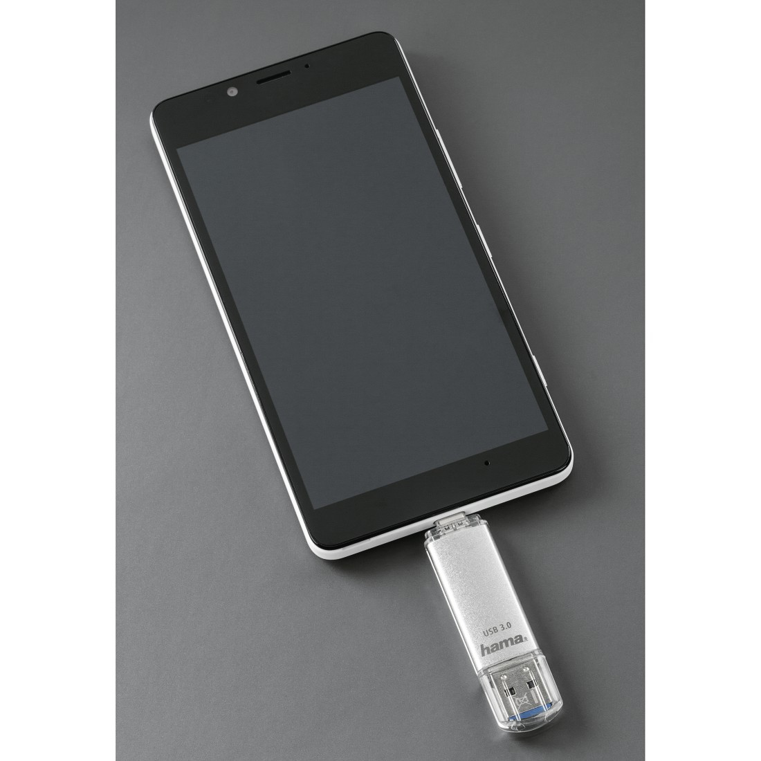 Czarny smartfon podłączony do srebrnego pendrive'a. Pendrive oznaczony 'USB 3.0 Hama'.