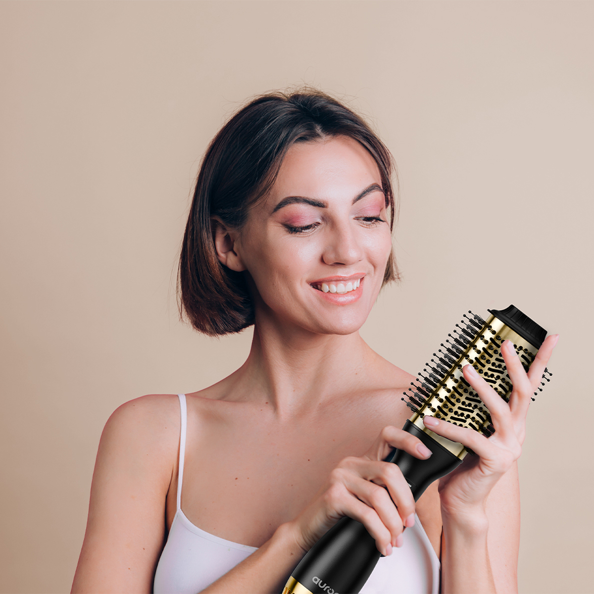 Femme tenant une brosse à coiffer noire et dorée, souriant à la caméra.