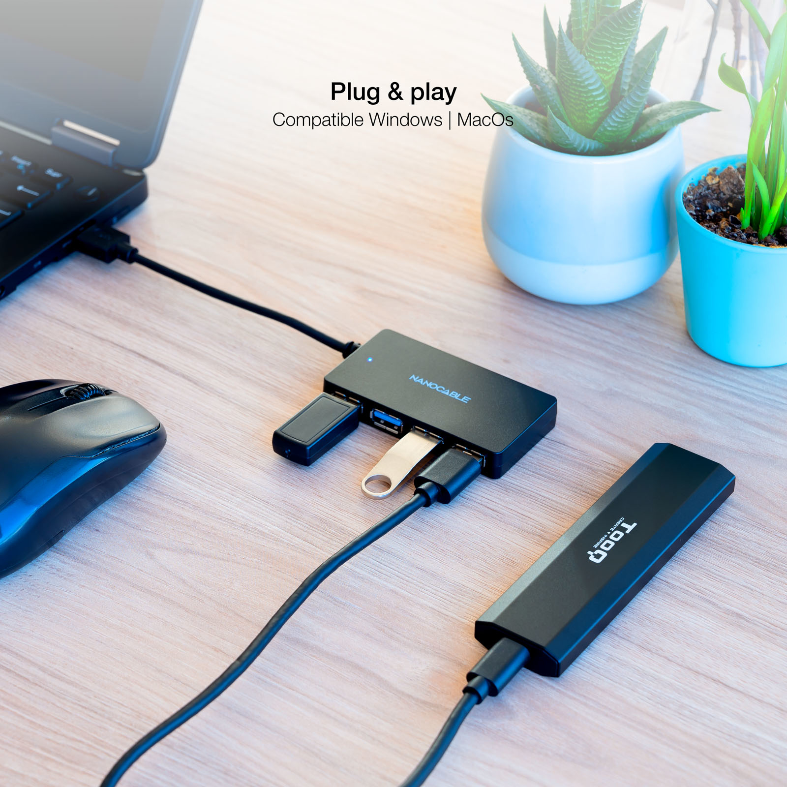 Concentrador USB negro con dispositivos conectados en un escritorio de madera con una laptop y una planta.