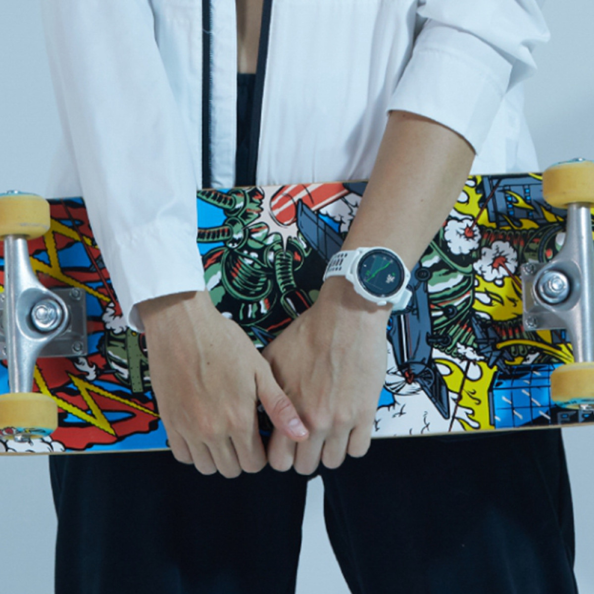 Una persona che tiene uno skateboard con un orologio bianco al polso. La persona indossa una camicia bianca e pantaloni neri.