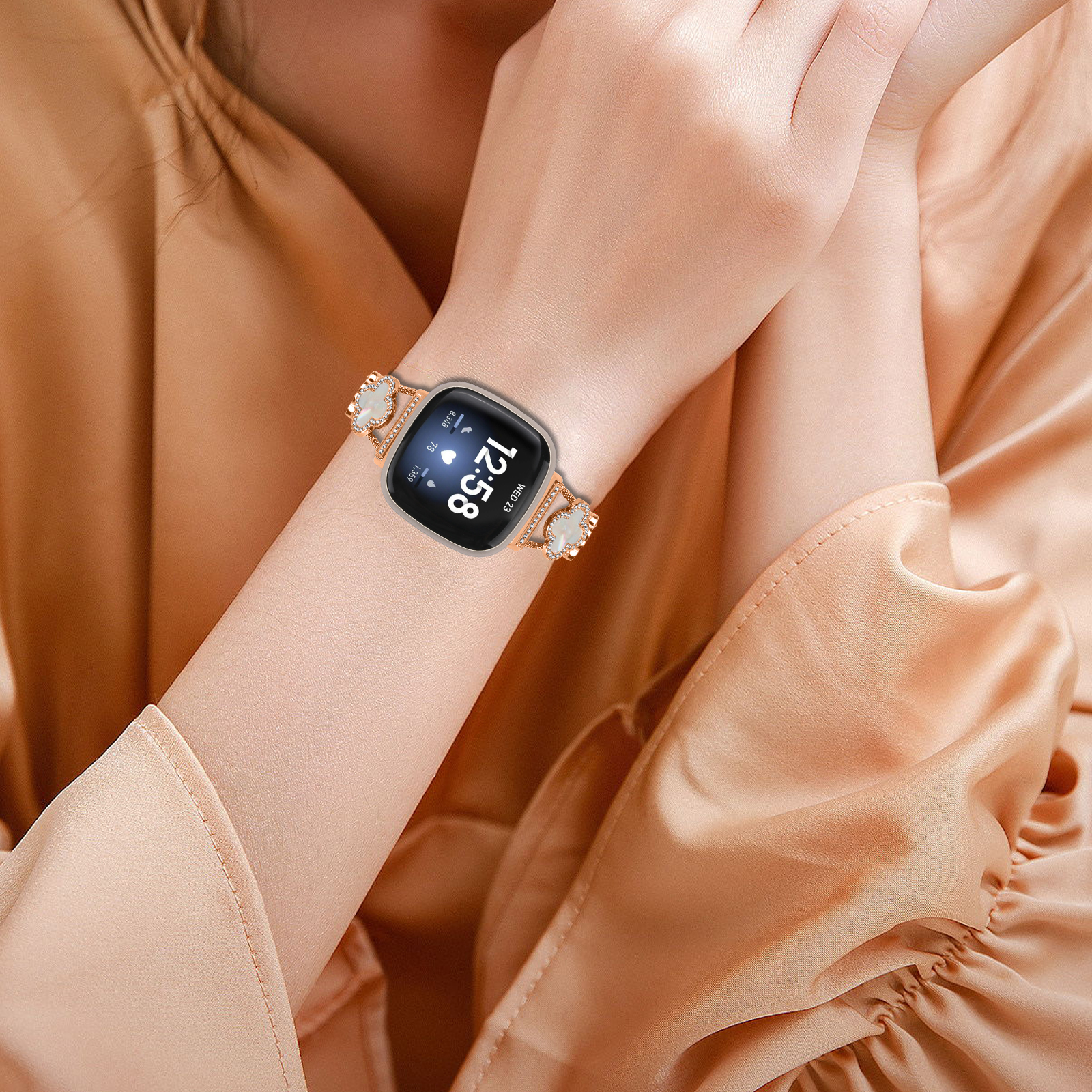 Handgelenk einer Frau mit roségoldener Smartwatch. Das Band ist mit Kristallen verziert.